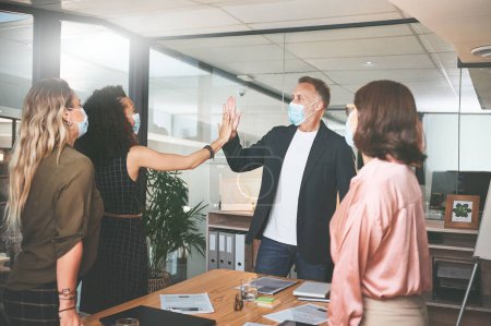Photo for Well done on completing the project. businesspeople standing together and giving each other a high five while wearing masks in the office - Royalty Free Image