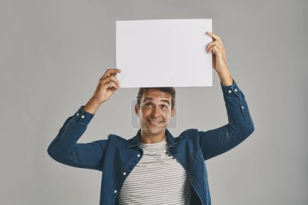Photo for Have you heard the big news. Studio shot of a young man holding a blank placard against a grey background - Royalty Free Image