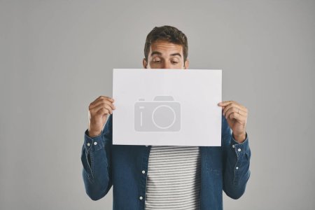 Photo for Would you look at that...Studio shot of a young man holding a blank placard against a grey background - Royalty Free Image