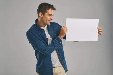 Photo for I think its an excellent message. Studio shot of a young man holding a blank placard against a grey background - Royalty Free Image