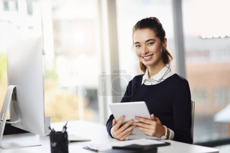 Foto de El éxito se gana, no se concede. Retrato de una atractiva joven empresaria sentada en su escritorio y usando una tableta en una oficina moderna - Imagen libre de derechos
