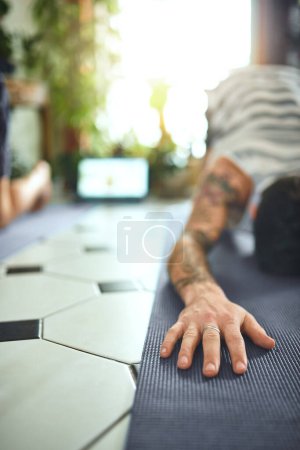 Foto de Estás a una sesión de yoga de volver a ti. un joven usando un portátil mientras pasa por una rutina de yoga en casa - Imagen libre de derechos