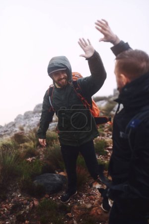 Téléchargez les photos : On est arrivés au sommet. deux amis masculins se donnant un high-five lors de randonnées dans les montagnes - en image libre de droit