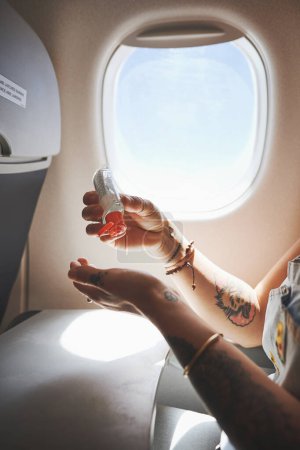 Foto de Protéjase a sí mismo y a otros. una mujer desinfectando sus manos en el avión - Imagen libre de derechos