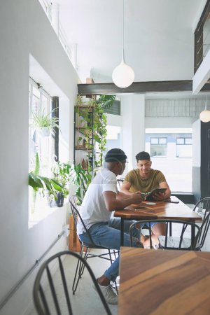 Photo for Coffee is the fuel that we need. Full length shot of two handsome friends sitting together and using a tablet during a discussion in a coffeeshop - Royalty Free Image