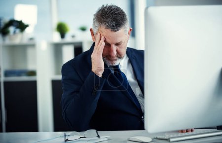 Photo for Its one of those days...a mature businessman experiencing a headache while working at his desk in a modern office - Royalty Free Image