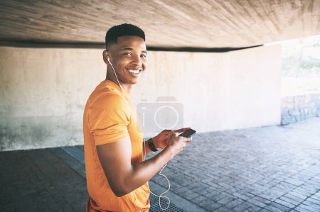 Photo for This is my kind of gym equipment. Portrait of a young man using a smartphone and earphones during a workout against an urban background - Royalty Free Image