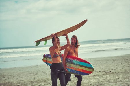 Téléchargez les photos : Surfer est toujours une bonne idée. un jeune couple marchant sur la plage avec leurs planches de surf - en image libre de droit