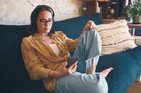 Foto de Algunos días son para moverte a tu ritmo. una mujer joven usando auriculares y un teléfono inteligente mientras se relaja en el sofá en casa - Imagen libre de derechos