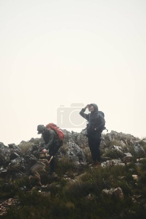 Foto de Le encanta hacer senderismo tanto como a nosotros. dos amigos y un perro de excursión en las montañas en un día de niebla - Imagen libre de derechos