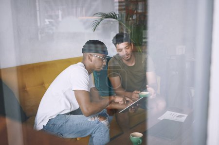 Téléchargez les photos : Discuter affaires dans notre café préféré. deux jeunes hommes discutant de quelque chose sur une tablette numérique tout en prenant un café ensemble - en image libre de droit