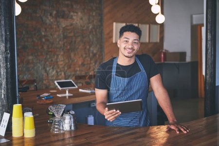 Photo for Business has bean nothing short of a success. a confident young man using a digital tablet while working in a cafe - Royalty Free Image