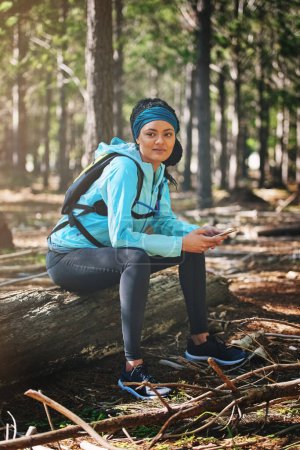 Photo for Everyday is a chance to get better. Full length shot of an athletic young woman sending a text while jogging in the woods - Royalty Free Image