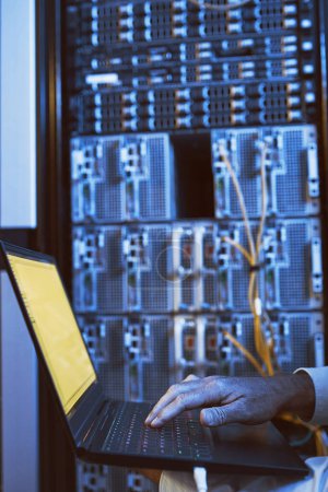 Photo for Lets diagnose and fix this quickly. Closeup shot of an unrecognisable man using a laptop while working in a server room - Royalty Free Image