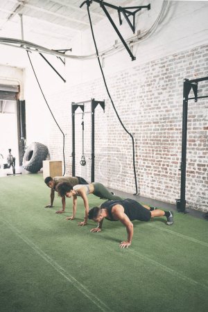 Photo for You push harder when youre part of something bigger. a fitness group doing push-ups at the gym - Royalty Free Image