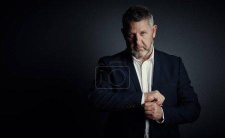 Photo for Its time to suit up. Studio portrait of a handsome mature businessman buttoning his sleeves while standing against a dark background - Royalty Free Image