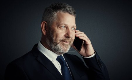 Photo for You have my attention. Studio shot of a handsome mature businessman looking thoughtful while making a call against a dark background - Royalty Free Image