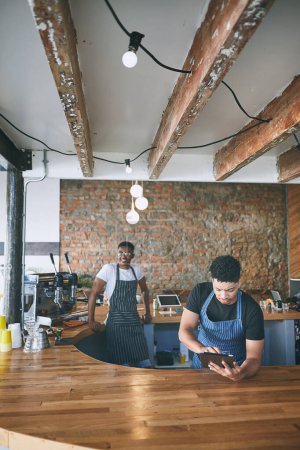 Foto de El trabajo duro hace que una pequeña empresa trabaje. dos jóvenes usando una tableta digital mientras trabajan en un café - Imagen libre de derechos