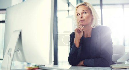 Foto de ¿Cómo puedo cambiar eso? una mujer de negocios reflexiva que trabaja en su escritorio en una oficina moderna - Imagen libre de derechos