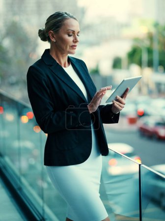 Foto de Llevando su trabajo afuera. una mujer de negocios madura parada afuera en el balcón de una oficina y usando una tableta digital - Imagen libre de derechos