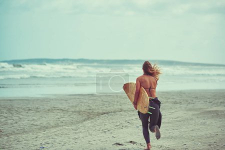 Téléchargez les photos : Passons à la prochaine vague. une jeune surfeuse portant sa planche de surf sur la plage - en image libre de droit