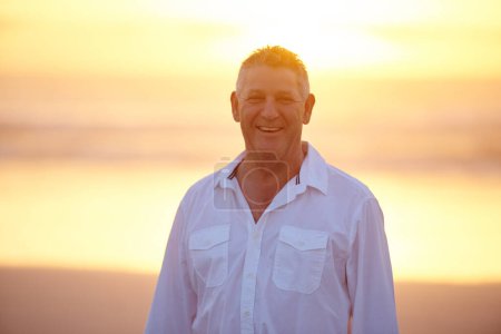 Téléchargez les photos : J'adore la plage. Portrait recadré d'un bel homme mature debout sur la plage au coucher du soleil - en image libre de droit