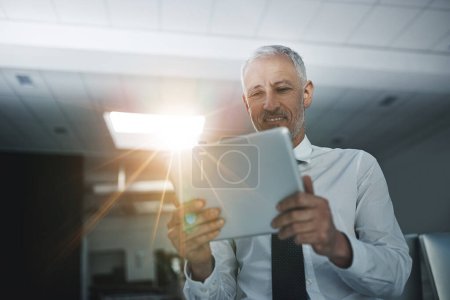 Foto de Es un ejecutivo experto en tecnología. un hombre de negocios parado en una oficina usando una tableta digital - Imagen libre de derechos