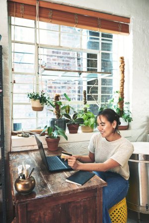 Photo for This would look great in my studio. an attractive young business owner sitting alone in her studio and using her laptop for online shopping - Royalty Free Image