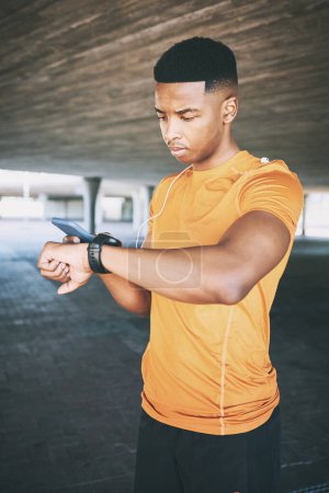 Photo for On track to peak fitness. a young man pairing his watch with a smartphone during a workout against an urban background - Royalty Free Image