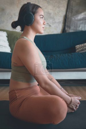 Photo for Music keeps her in a calm state of mind. a young wearing headphones while exercising at home - Royalty Free Image