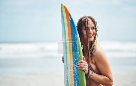 Foto de No puedo esperar a golpear el agua. una joven atractiva parada en una playa con una tabla de surf - Imagen libre de derechos