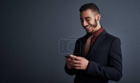 Foto de Las buenas noticias siempre le hacen sonreír. Imagen de estudio de un joven hombre de negocios con estilo que envía un mensaje de texto mientras está de pie sobre un fondo gris - Imagen libre de derechos