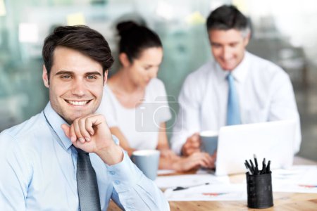 Photo for Comfortable in his career. Smiling young businessman sitting in a group meeting - Royalty Free Image