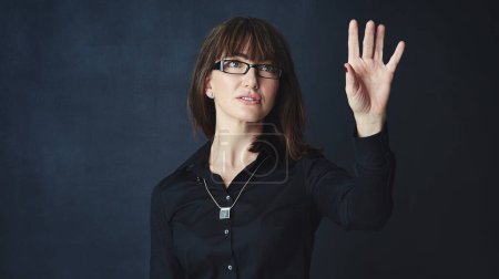 Photo for Making it easier to see the future, today. Studio shot of a businesswoman connecting to a user interface with her finger against a dark background - Royalty Free Image