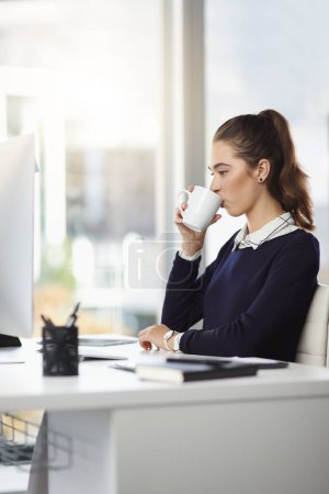 Téléchargez les photos : Juste un petit pick-me-up. une jolie jeune femme d'affaires assise à son bureau et dégustant une tasse de café dans un bureau moderne - en image libre de droit