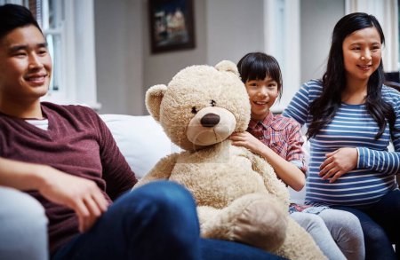 Photo for I love my teddy. Cropped portrait of a little girl sitting on the sofa with her teddybear between her parents - Royalty Free Image