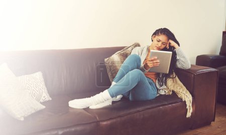 Foto de Me atraganto viendo porque puedo. una mujer joven usando su tableta mientras se relaja en casa - Imagen libre de derechos