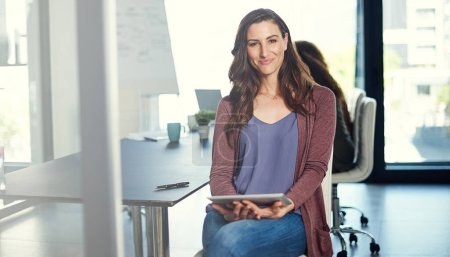 Foto de Me ayuda a mantener el control de los negocios. Retrato de una joven empresaria trabajando en una tableta digital con sus colegas de fondo - Imagen libre de derechos