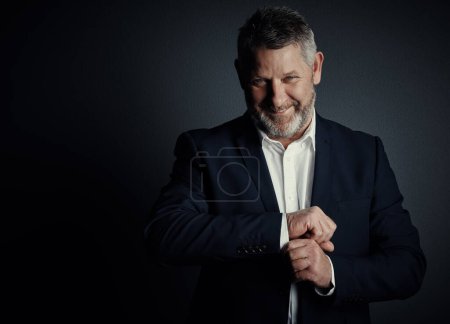 Photo for Hes got bags of confidence. Studio portrait of a handsome mature businessman buttoning his sleeves while standing against a dark background - Royalty Free Image