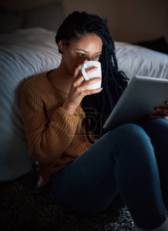 Foto de De qué se tratan las noches tranquilas. una joven relajada bebiendo café y usando una tableta digital durante la noche en casa - Imagen libre de derechos