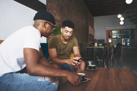 Foto de Déjame mostrarte una foto... hombres discutiendo algo en un celular mientras están sentados juntos en una cafetería - Imagen libre de derechos