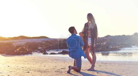 Téléchargez les photos : Il y a quelque chose que je voulais te demander. un jeune homme tenant sa main de copines sur le genou plié à la plage - en image libre de droit