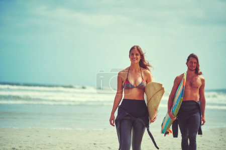 Téléchargez les photos : Nous pouvons supporter les eaux orageuses. un jeune couple marchant sur la plage avec leurs planches de surf - en image libre de droit
