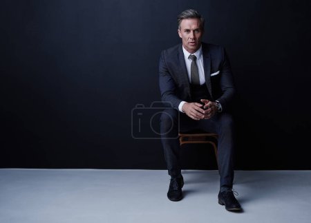 Photo for I dont settle for less. Studio portrait of a mature businessman sitting on a chair against a dark background - Royalty Free Image