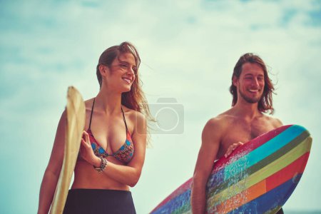 Téléchargez les photos : Le surf nous rapproche. un jeune couple marchant sur la plage avec leurs planches de surf - en image libre de droit