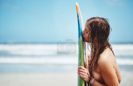 Téléchargez les photos : Il est temps d'attraper quelques vagues. une jolie jeune femme debout sur une plage embrassant sa planche de surf - en image libre de droit