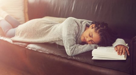 Foto de Tener un merecido descanso. una joven dormida en su sofá con un libro delante de ella - Imagen libre de derechos
