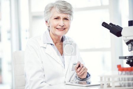Foto de La confianza es importante en esta industria. Retrato de una alegre científica anciana tomando notas mientras mira a la cámara y sonríe en un laboratorio - Imagen libre de derechos