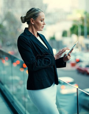 Foto de Apoyar el éxito empresarial con tecnología inteligente. una mujer de negocios madura parada afuera en el balcón de una oficina y usando una tableta digital - Imagen libre de derechos