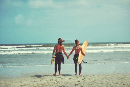Téléchargez les photos : Objectifs relationnels. un jeune couple marchant sur la plage avec leurs planches de surf - en image libre de droit